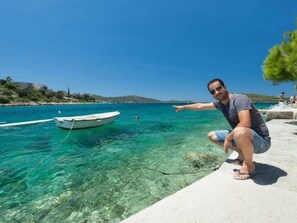 A man pointing towards a boat anchored in clear blue water, with a beach and a distant shoreline in the background. - in Dvornica mit Gepflegtem Garten by Interhome (Podorljak)