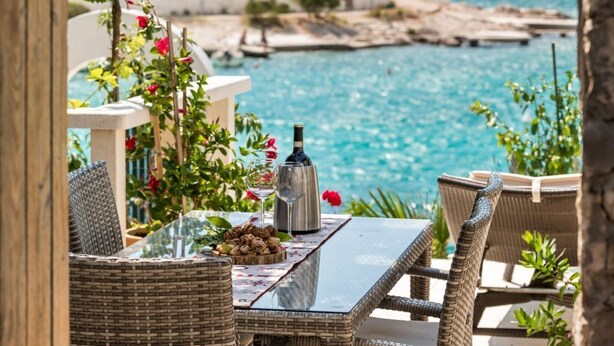 An outdoor dining area with wicker furniture, a table with a bottle and glasses, and a view of the sea and rocky landscape. - mit Blick auf das Wasser by Interhome (Podorljak)