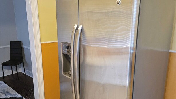 Een koelkast van roestvrij staal in een keuken met gele wanden en een betegelde vloer.