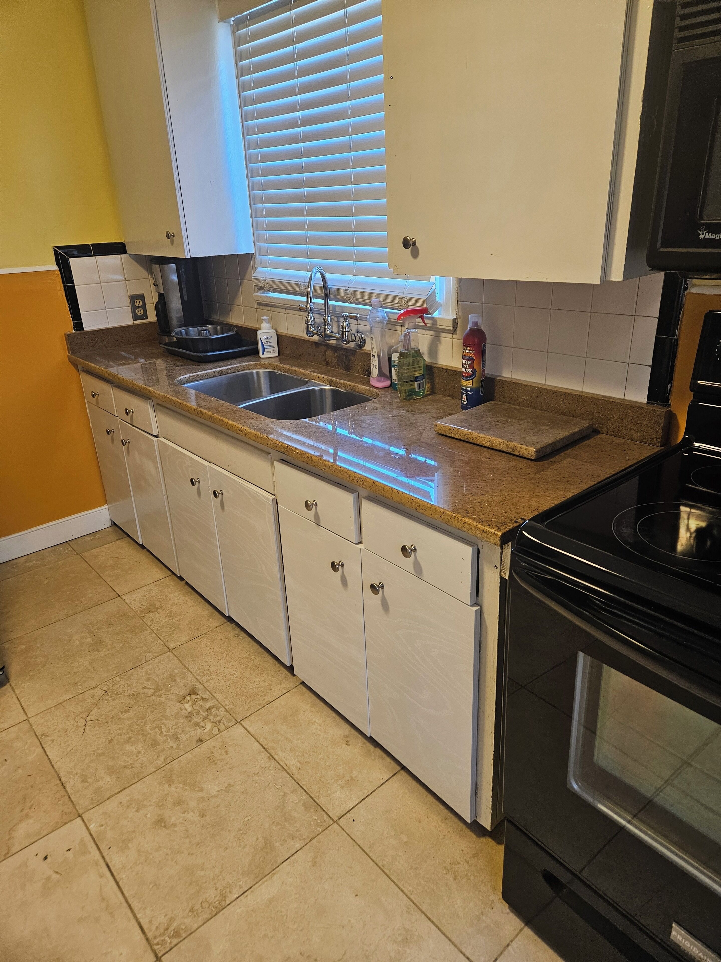 A kitchen with white cabinets, a granite countertop, a sink, a stove, and a window with blinds.