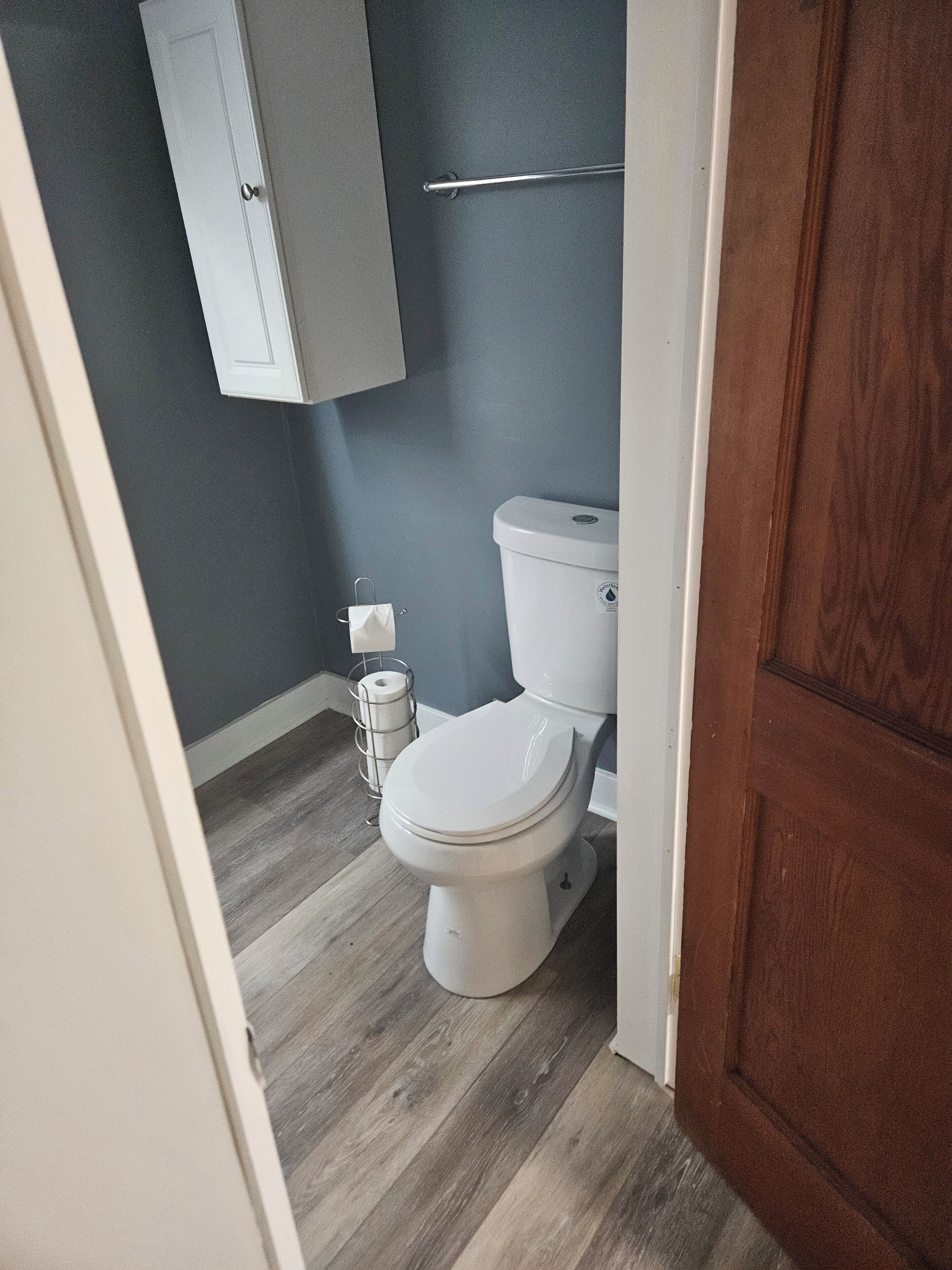 Un bagno piccolo con il water, un pavimento in legno e un armadietto sopra il water.