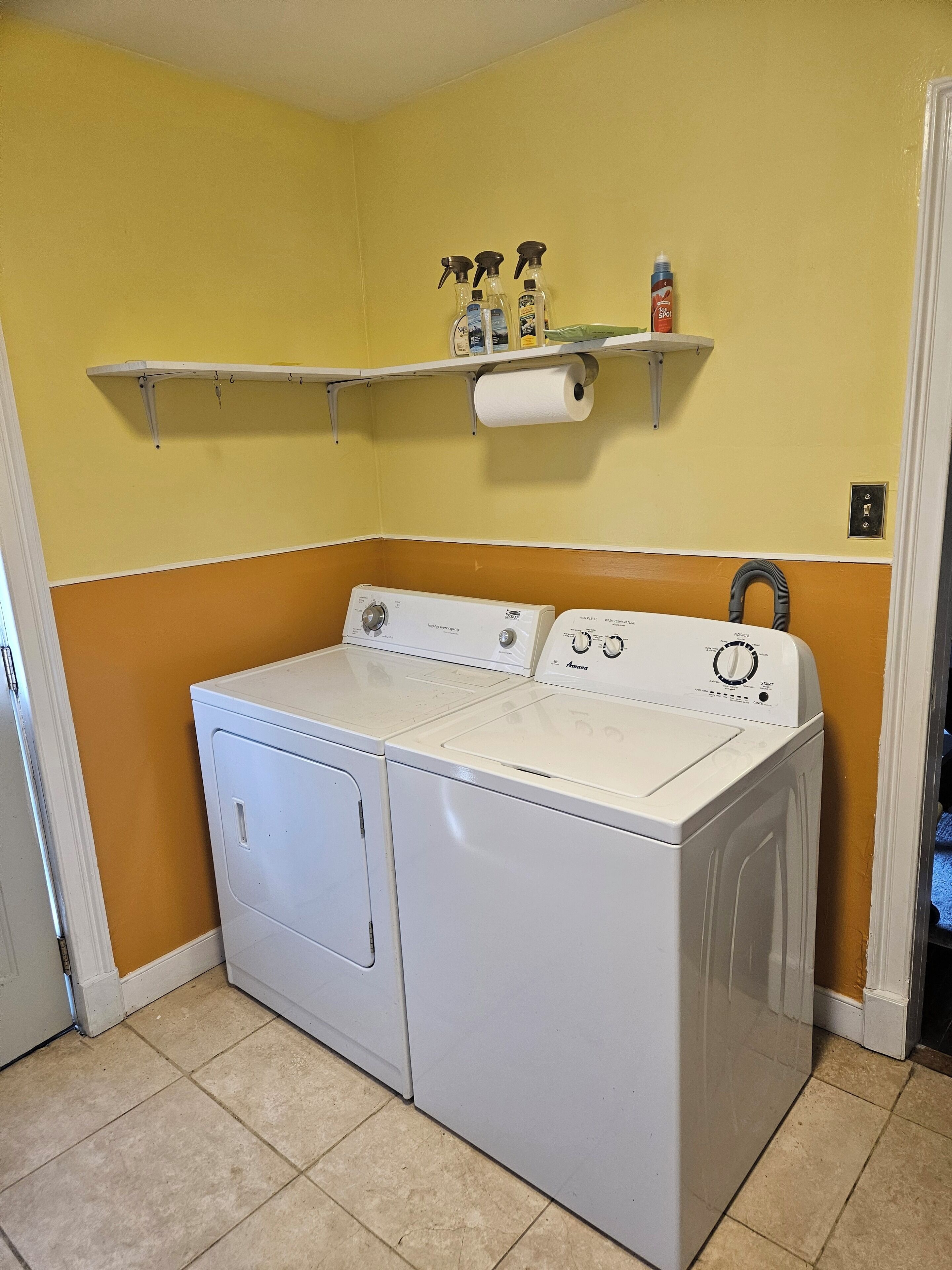 A laundry room with a front-loading washer and dryer, a shelf with cleaning supplies, and a roll of paper towels.