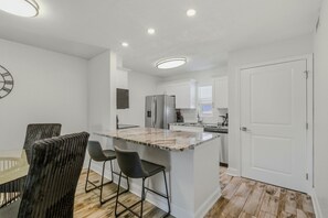 A modern kitchen with a marble island, bar stools, and a dining table with chairs. - Modern 2BR in South Tampa with Pool, Parking & Workspace (Tampa)