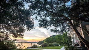 Une zone herbeuse avec un sentier menant à un plan d’eau, entourée d’arbres et d’un bâtiment doté d’un toit en pente.