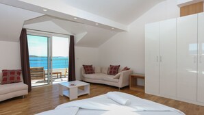 Une chambre moderne avec un lit, un canapé, une petite table et une armoire. Elle dispose d’un balcon avec vue sur la mer.