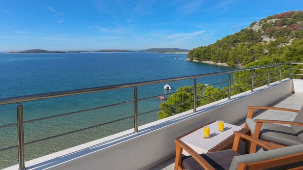 Un balcon offrant une vue dégagée sur la mer, une table avec deux verres et des chaises en bois.