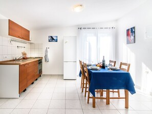 A modern kitchen with wooden cabinets, a white refrigerator, and a dining area with a blue tablecloth. - "Sunny Apartmen" direkt am Strand by Interhome (Tisno)