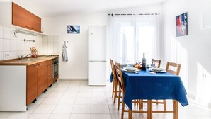 A modern kitchen with wooden cabinets, a white refrigerator, and a dining area with a blue tablecloth. - in Tisno mit Terrasse und Grill by Interhome (Tisno)