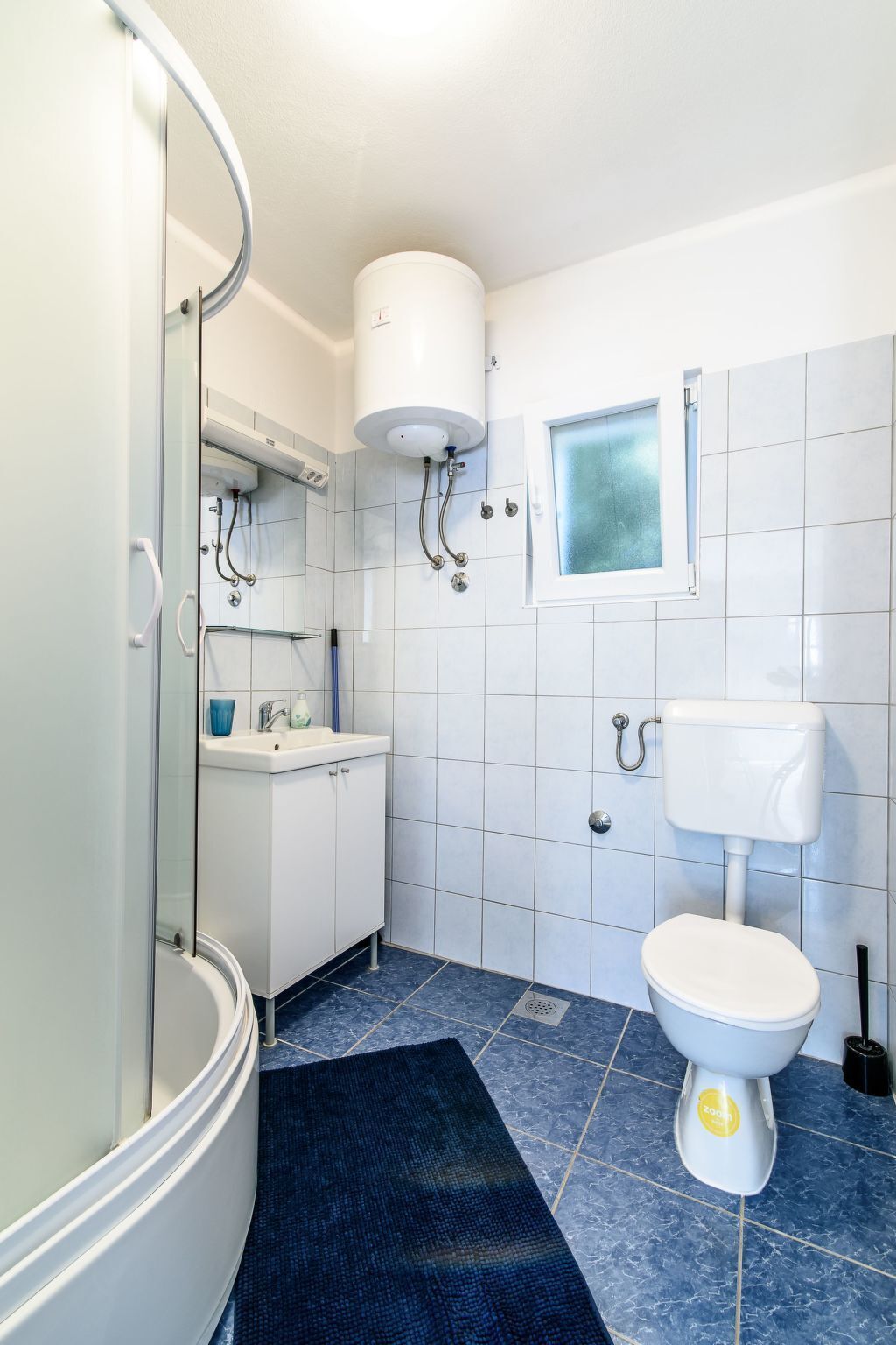 A bathroom with a glass shower enclosure, a white sink, a toilet, and a window.