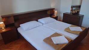 Een tweepersoonsbed met twee kussens, een houten hoofdbord, een nachtkastje met lamp en een dressoir met spiegel.