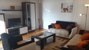 Een woonkamer met een bank, fauteuils, een salontafel, een televisie en een kast.