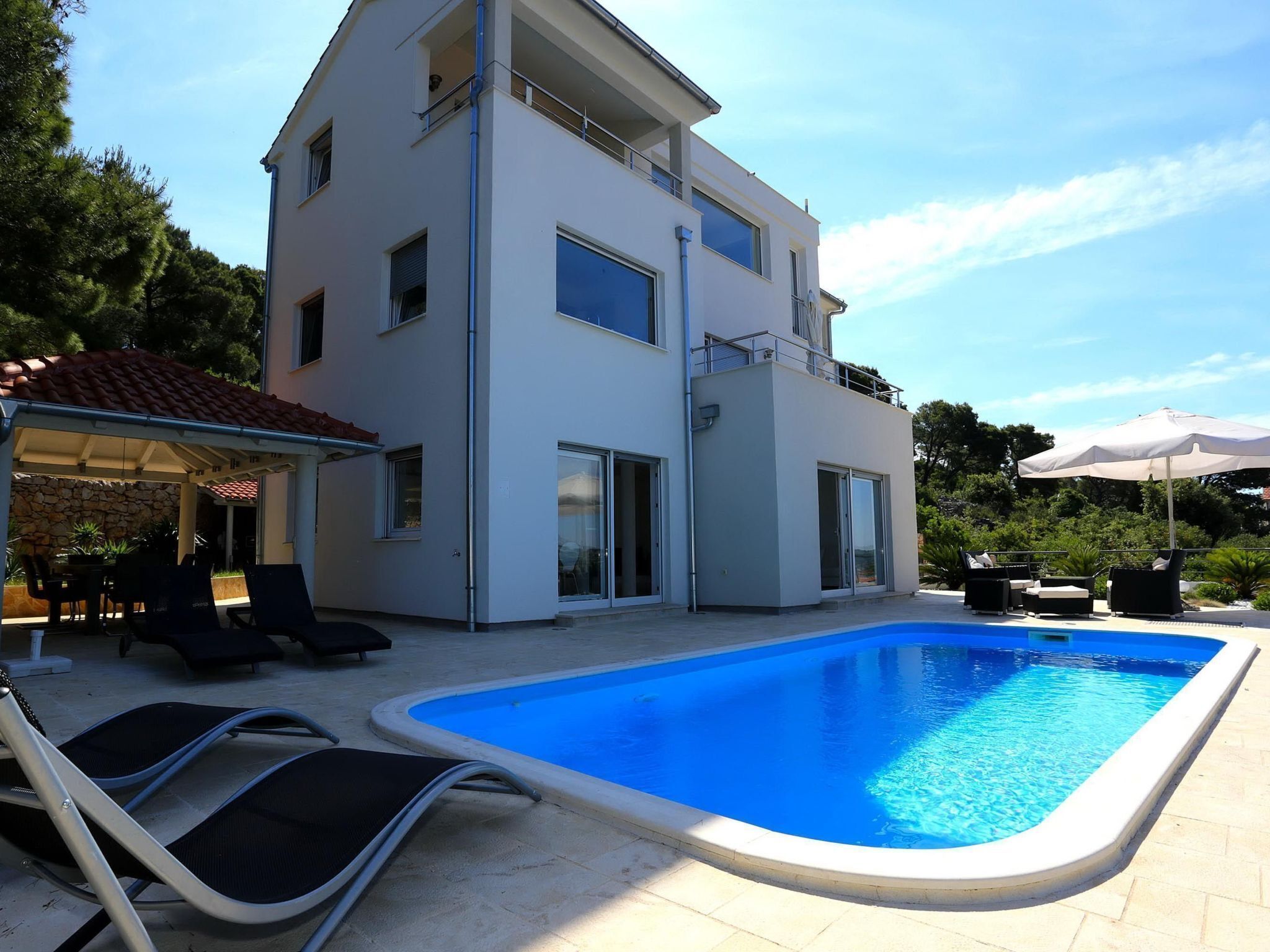 A modern two-story house with a swimming pool, outdoor seating, and a covered patio area.