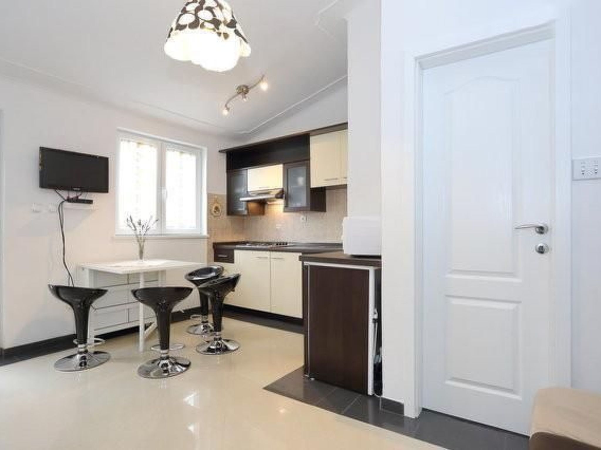 A modern kitchen with white cabinets, a black countertop, and a built-in oven. There are three black bar stools and a white dining table.
