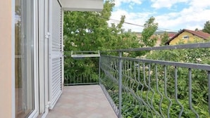 En balkon med gelænder, flisegulv og udsigt til grønt og bygninger i baggrunden.