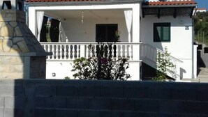 Uma casa de dois andares com telhado de telhas vermelhas, uma varanda com balaústres brancos e uma antena parabólica.