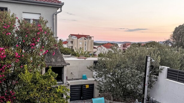 Um terraço no telhado com mesa e cadeiras, rodeado por vegetação e edifícios.