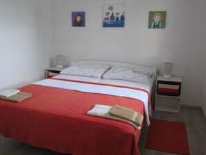 A neatly made bed with a red and white bedspread, two pillows, and two bedside tables with lamps. There are three wall-mounted pictures above the bed. - mit überdachter Terrasse und Meerblick by Interhome (Drage)