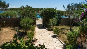 Un sendero de piedra conduce a un área de piscina rodeada de follaje y una pared de piedra.