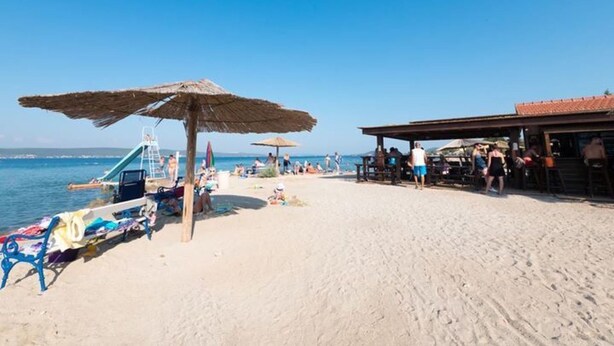 En strand med ett parasoll av halmtak, ett livräddartorn och en byggnad med ett tak täckt av tegelpannor.