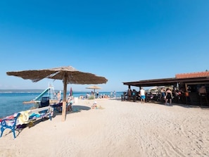 Ein Strand mit einem Reetdach-Sonnenschirm, einem Rettungsturm und einem Gebäude mit Ziegeldach.