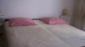 Una cama con un edredón blanco texturizado y dos almohadas rosas con estampado floral.