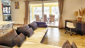 En moderne stue med sofa, spisebord og et køkken, der kan ses gennem en åben dør.