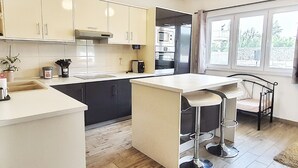 Et moderne køkken med en central ø, barstole og udsigt til det frie gennem store vinduer.
