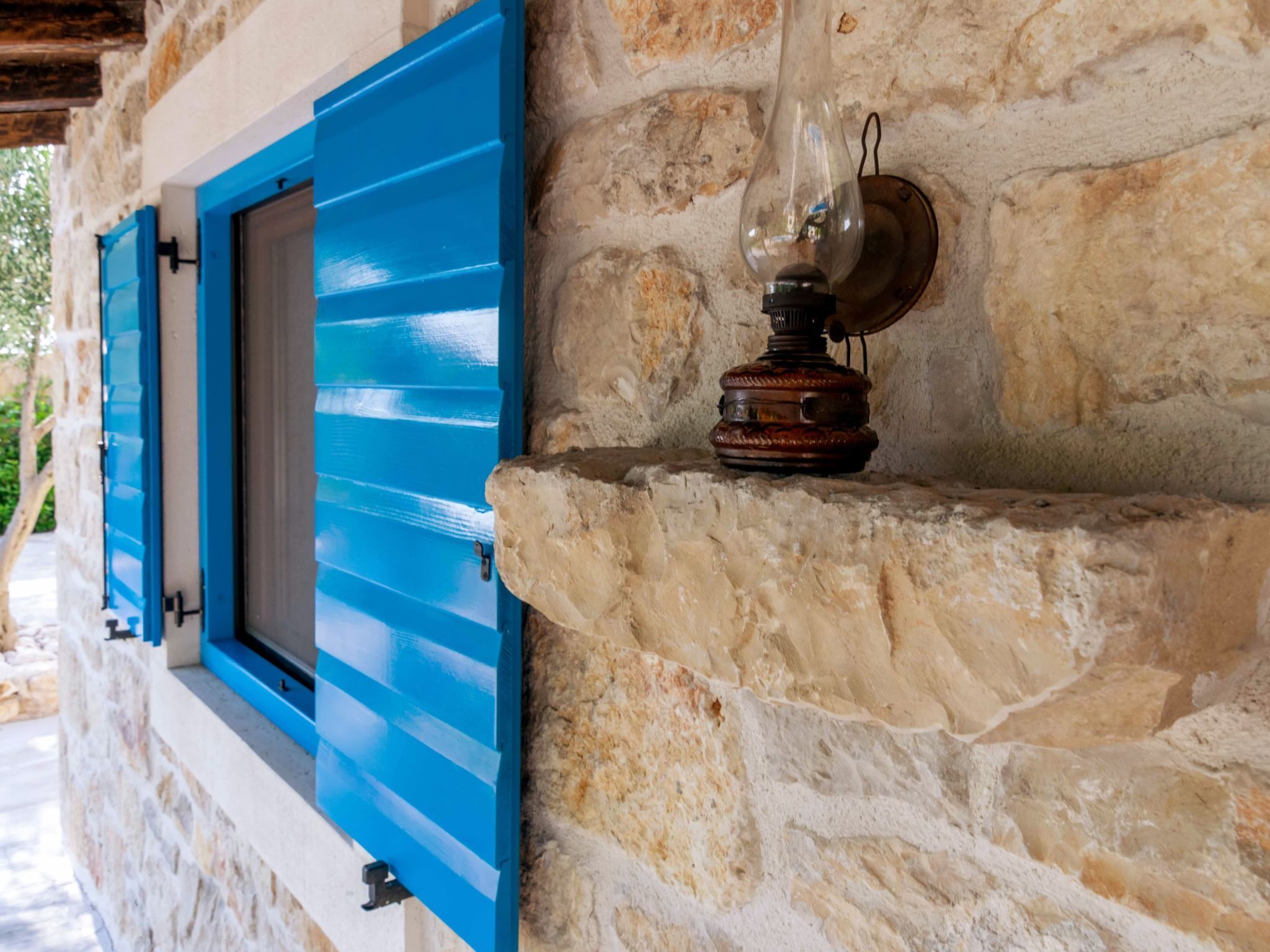 A stone wall with a blue shuttered window and a vintage-style wall sconce.