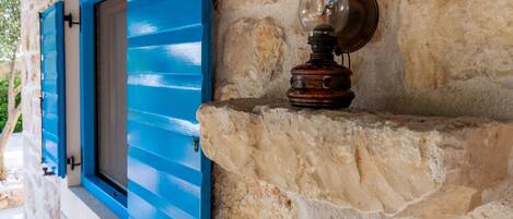 A stone wall with a blue shuttered window and a vintage-style wall sconce.