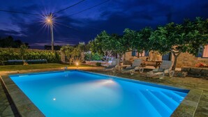 Una piscina rectangular amb un marc de pedra, envoltada per un pati amb gandules i una paret de pedra.