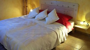 Un lit bien fait, avec une literie blanche et des oreillers rouges, une tête de lit en bois et une table de chevet avec une lampe.