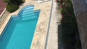 Una piscina d'aigua transparent de color blau, envolta d'àmfores de pedra i un marc de pedra.