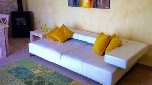 Ein Wohnzimmer mit einem weißen Sofa, zwei gelben Kissen, einem farbenfrohen abstrakten Gemälde, einem schwarzen Kamin und einer Steinwand.