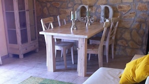 Ein gemütliches Zimmer mit Steinwand, einem Holzespeisetisch mit Stühlen und einem cremefarbenen Sofa mit gelben Kissen.