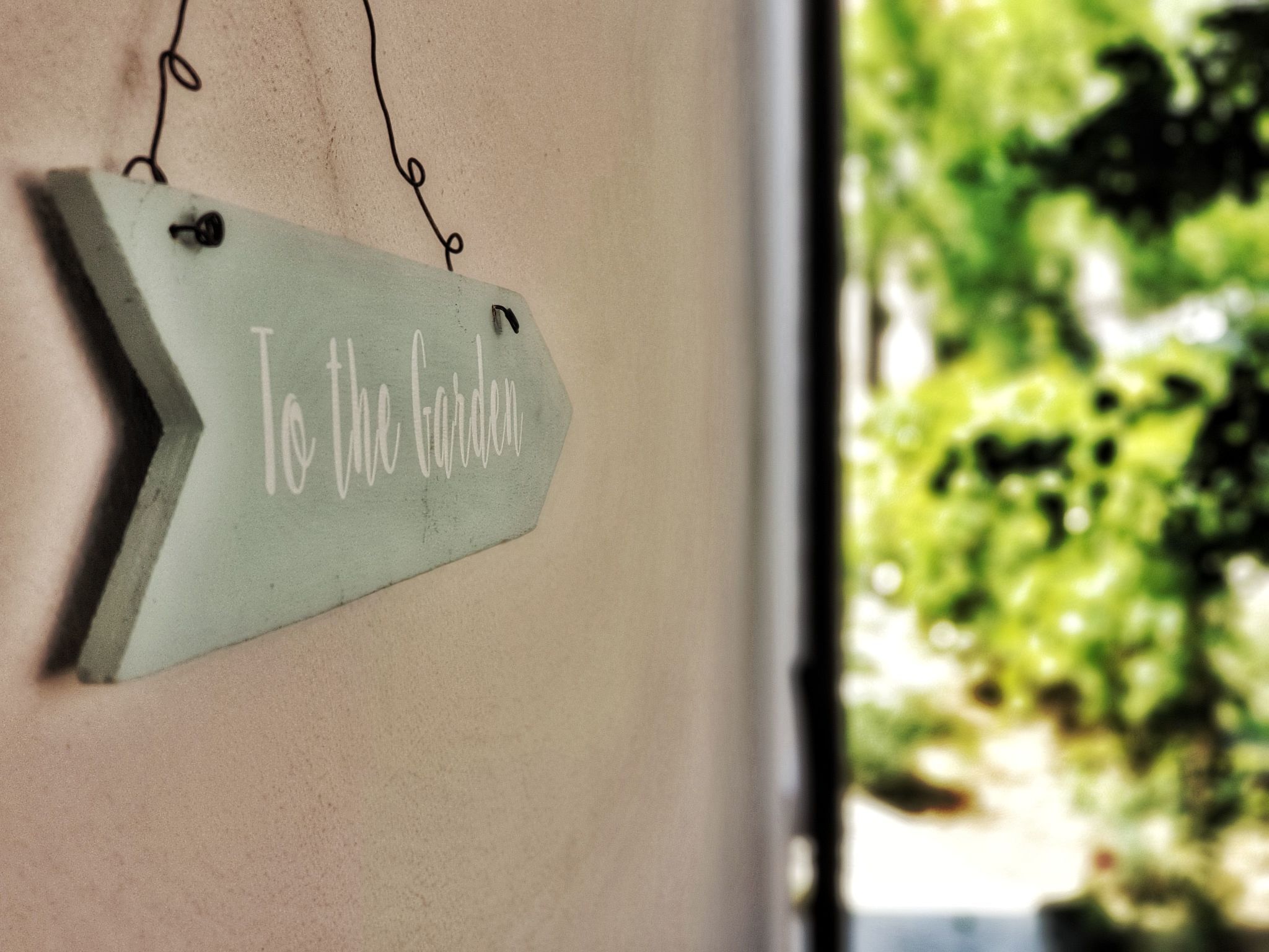 A sign with the text "To the Garden" hanging on a wall.