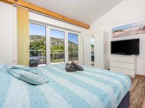 Ein Schlafzimmer mit Bett, Fernseher und einem Balkon mit Meerblick.
