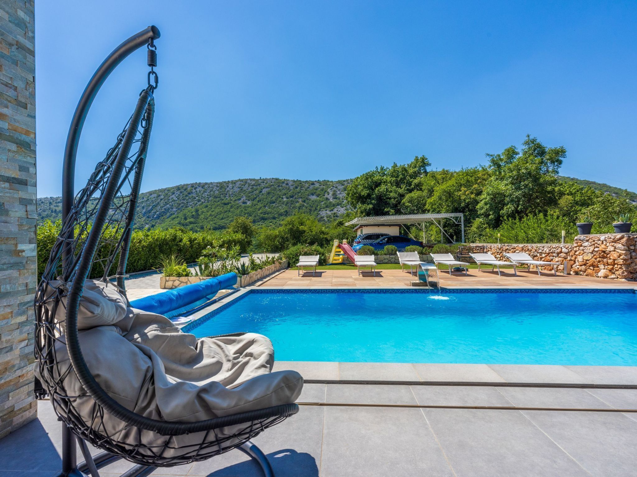 A pool area with a swing chair, lounge chairs, and a view of a mountain.