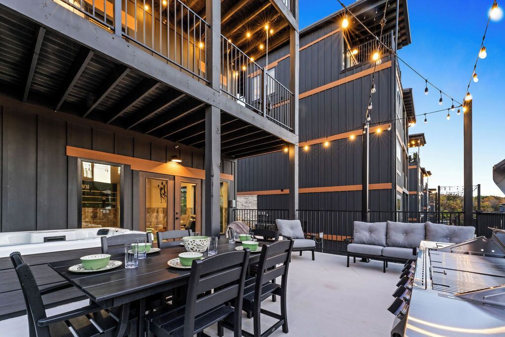 A modern outdoor dining area with a table set for two, surrounded by chairs.