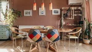 Uma sala de jantar com mesa e cadeiras de madeira, luminárias pendentes e quadros nas paredes.