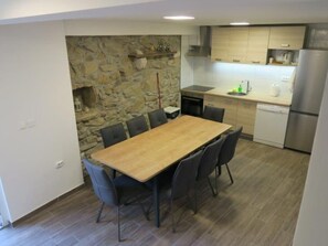 A compact kitchen with a stone accent wall, a wooden dining table with chairs, and modern appliances. - Renoviertes Ferienhaus in Baska mit Terrasse by Interhome (Krk/Baška)