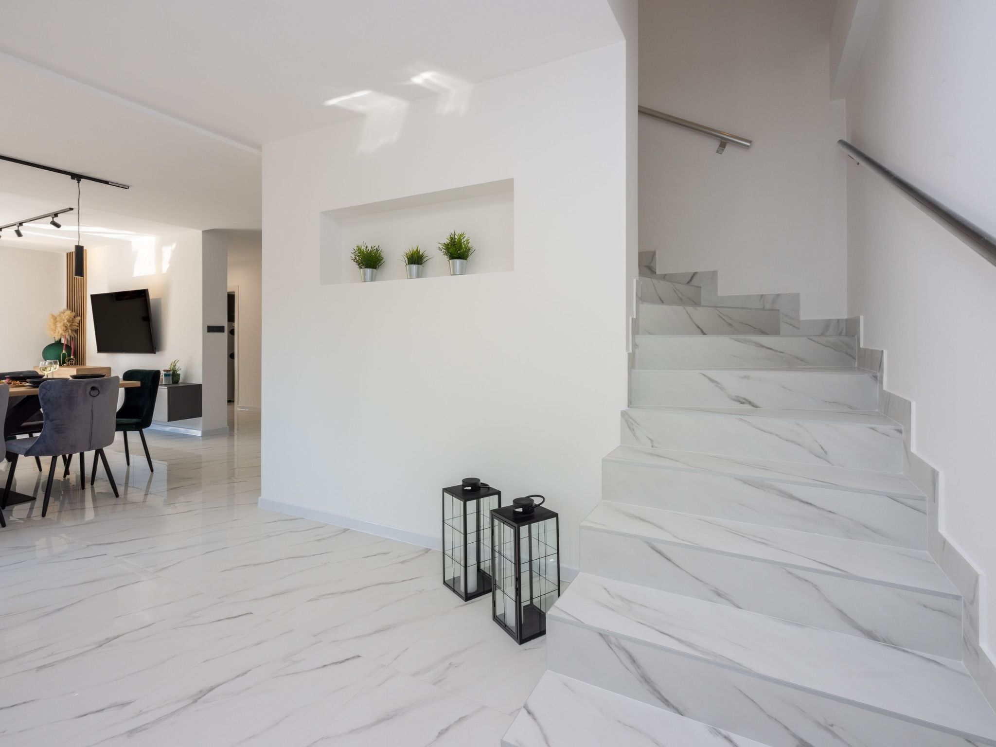 A modern interior with a marble staircase, a dining area with a table and chairs, and a wall-mounted TV.