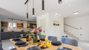 Ett modernt matområde med ett träbord dukat för frukost, med tallrikar, bestick och en vas med blommor.