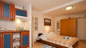 A compact bedroom with a bed, a small bedside table, a wardrobe, and a kitchenette area with cabinets and a stove. - Studio in einem traditionellen Steinhaus, in Baska by Interhome (Krk/Baška)