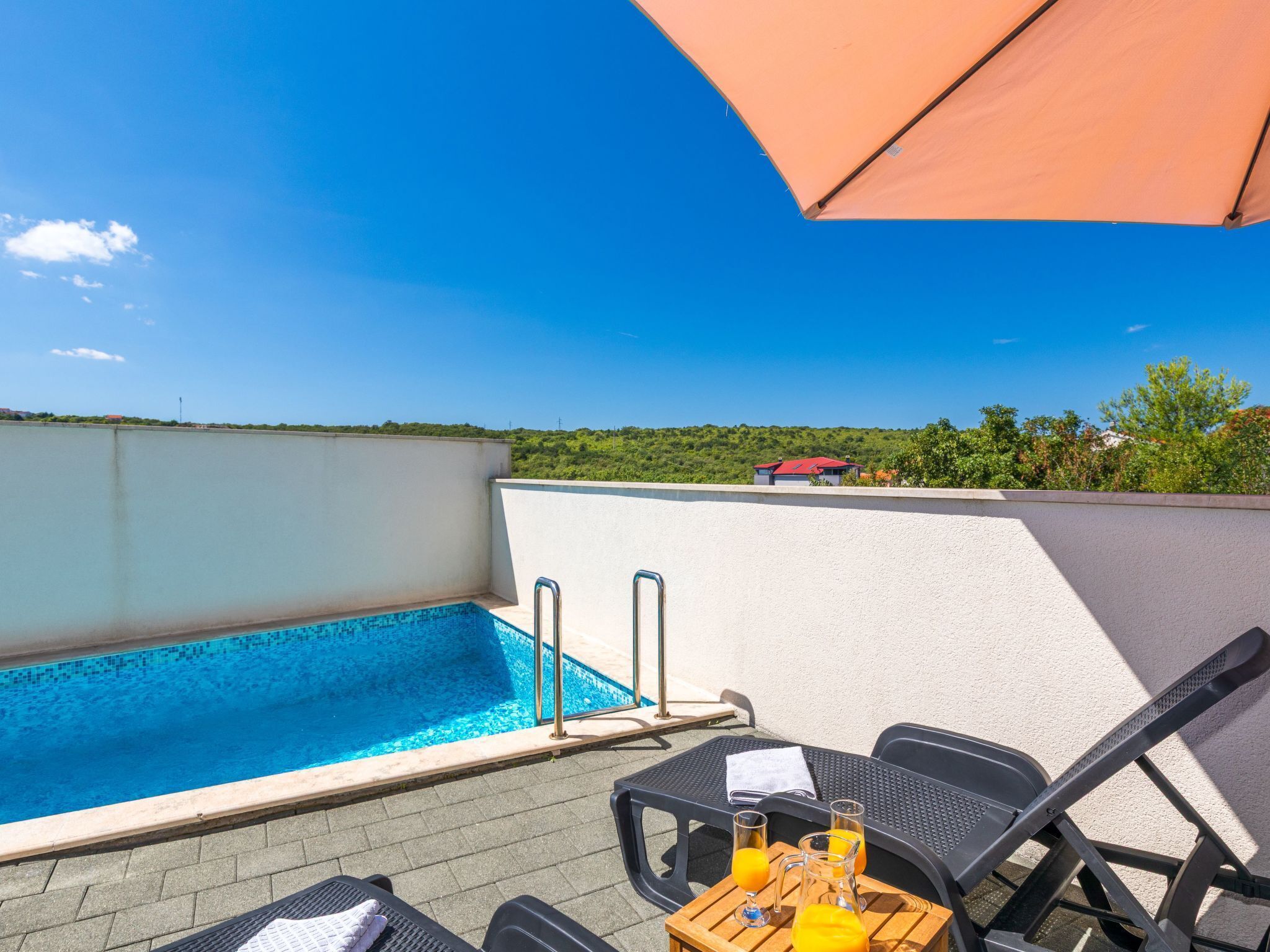 Área de piscina no terraço com vista desobstruída para o mar, piscina, espreguiçadeiras e uma mesa com bebidas.