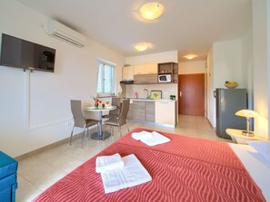 Habitación de hotel pequeña con cama, kitchenette, comedor con mesa y sillas, y televisor montado en la pared.