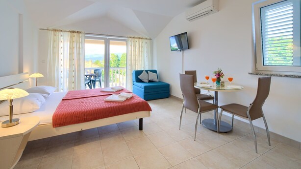 Ein Hotelzimmer mit Bett, Schreibtisch, Stuhl, einem Tisch mit Getränken, einem Fernseher und einem Balkon mit Blick.