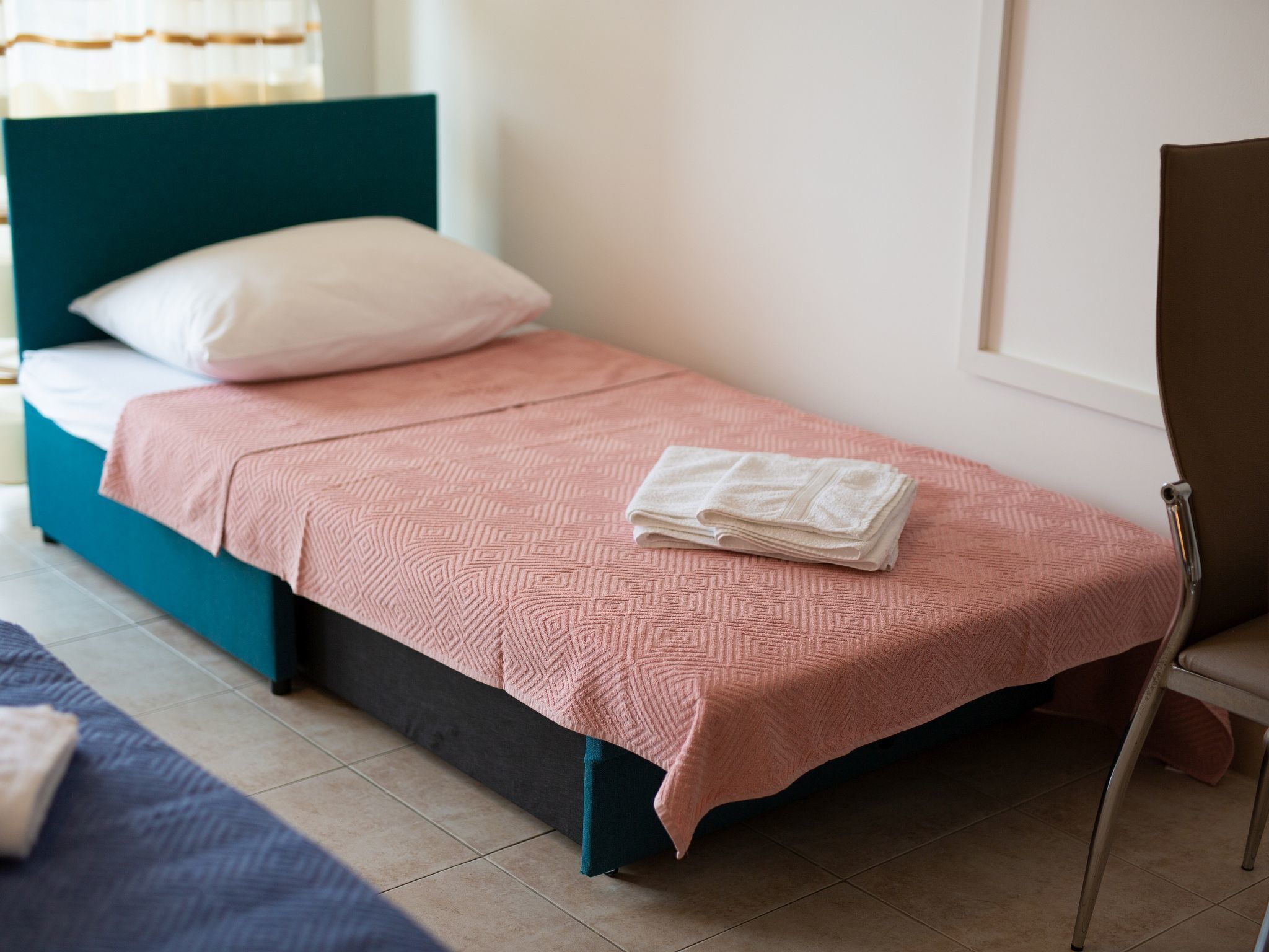 Ein Einzelbett mit einer rosa geblümten Bettdecke und einem gefalteten weißen Handtuch.