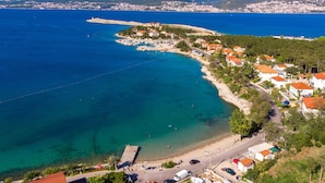 Vue aérienne d’une ville côtière avec une plage, des eaux d’un bleu limpide et un paysage montagneux en arrière-plan.