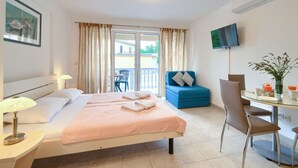 Ein Hotelzimmer mit Bett, Schreibtisch, Stuhl, Fernseher und einem Balkon mit Vorhängen.