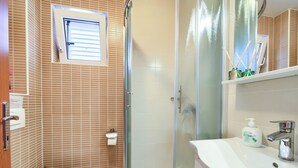Ein Badezimmer mit Toilette, einer gläsernen Duschkabine und einem Waschtisch mit Waschbecken und Spiegel.
